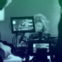 Photo of a video camera filming a scene in the background. We are looking into the camera as if we are operating it, and the background scene is slightly out of focus.